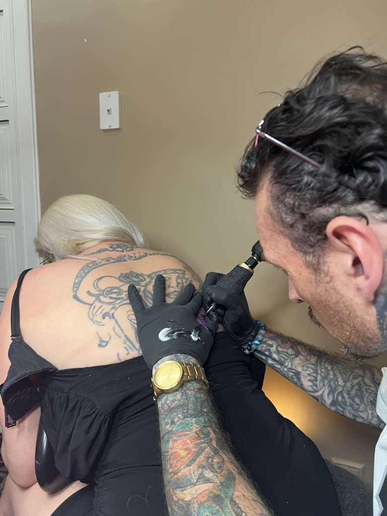 Joshua Cole tattoos upper back beside faded blue portrait on blonde client offsite — Joshua Cole…, Work of Art Tattoo & Piercing, Las Vegas