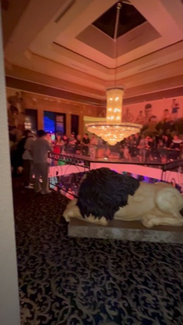 Crowd gathers on balcony above lion statue beneath crystal chandelier at Vegas venue — Joshua…, Work of Art Tattoo & Piercing, Las Vegas