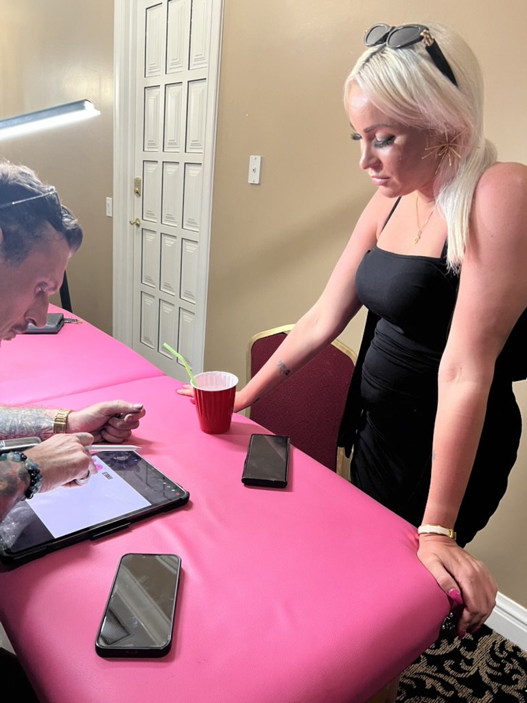 Blonde client watches Joshua Cole draw tattoo design on tablet — Joshua Cole offsite booking…, Work of Art Tattoo & Piercing, Las Vegas