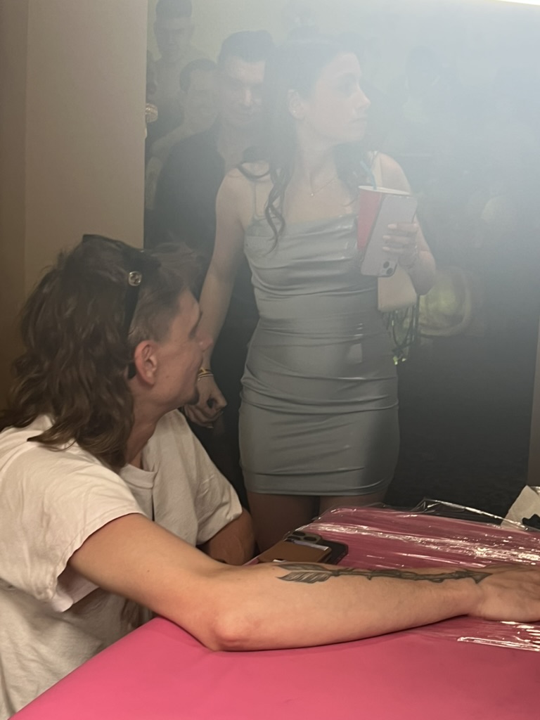 Client displays finished black arrow forearm tattoo at pink-covered offsite event table — Joshua…, Work of Art Tattoo & Piercing, Las Vegas
