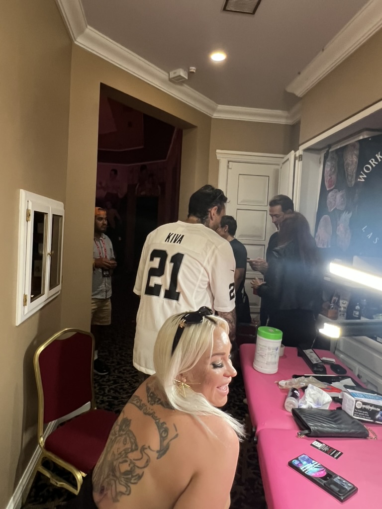 Blonde client turns showing finished ornate back tattoo at pink offsite event table — Joshua…, Work of Art Tattoo & Piercing, Las Vegas