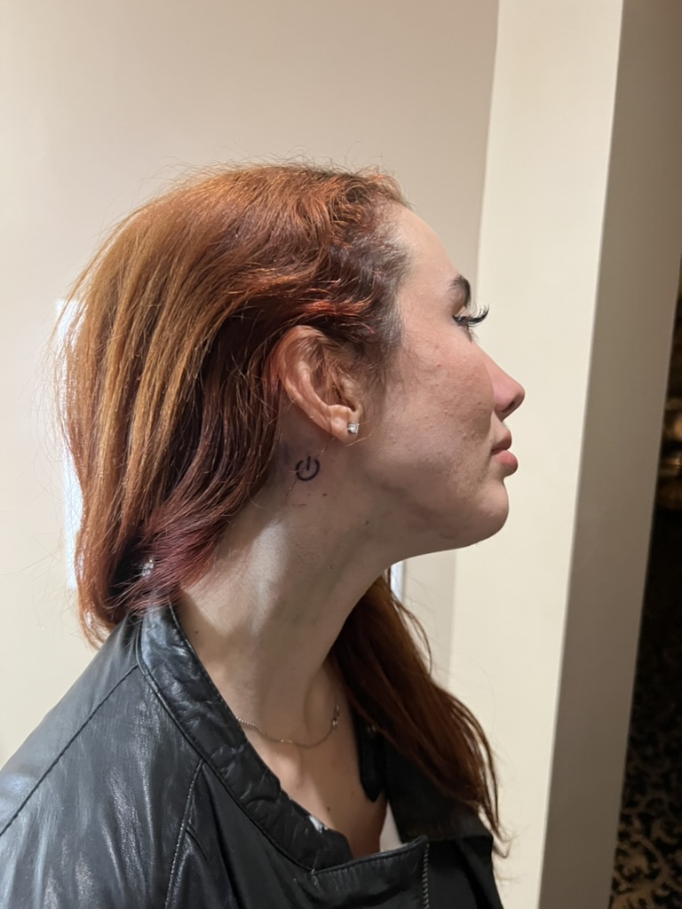 Fresh black power-button neck tattoo behind red-haired client's ear, finished offsite — Joshua…, Work of Art Tattoo & Piercing, Las Vegas