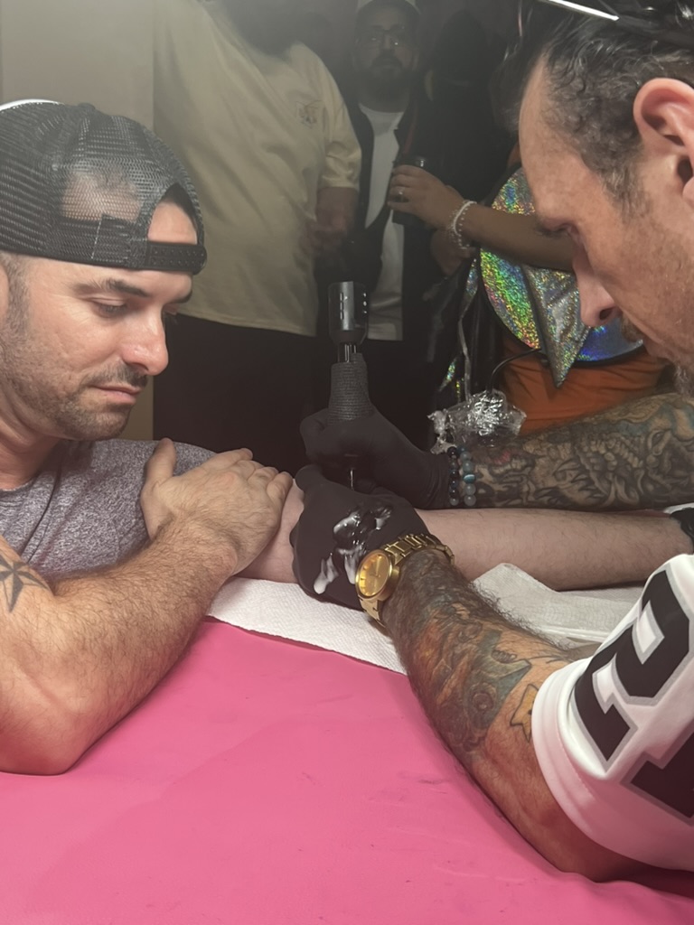 Joshua Cole tattoos client's inner forearm as onlookers watch at pink offsite station — Joshua…, Work of Art Tattoo & Piercing, Las Vegas