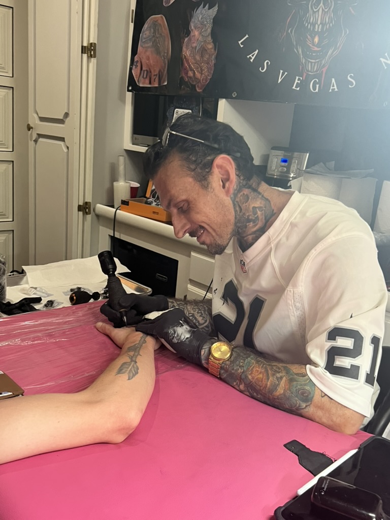 Joshua Cole tattoos back of hand on pink table; client has arrow forearm tattoo — Joshua Cole…, Work of Art Tattoo & Piercing, Las Vegas