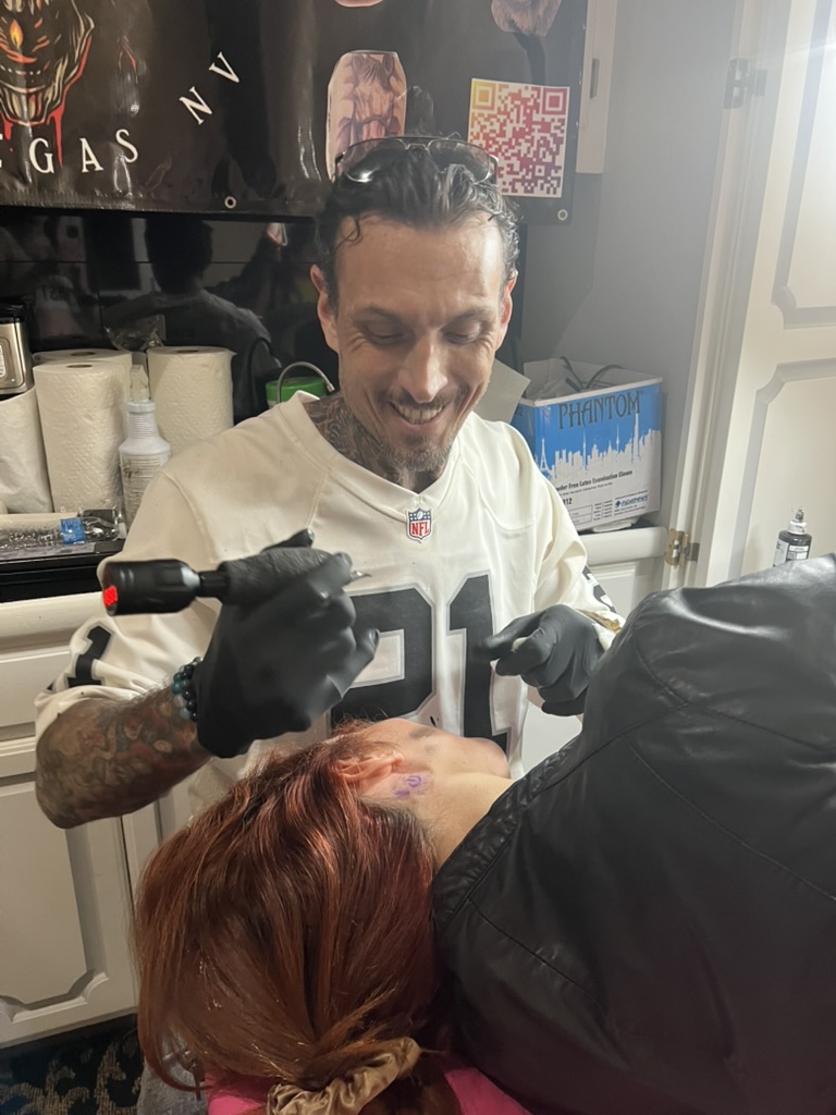 Joshua Cole smiles, machine ready behind client's ear stencil — Joshua Cole offsite booking…, Work of Art Tattoo & Piercing, Las Vegas
