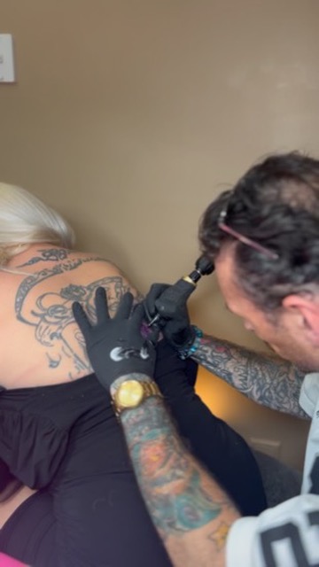 Joshua Cole inks ornate black-grey back tattoo on blonde client leaning forward — Joshua Cole…, Work of Art Tattoo & Piercing, Las Vegas