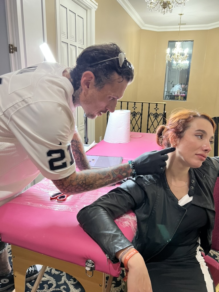 Joshua Cole marks neck spot behind client's ear at pink portable table — Joshua Cole offsite…, Work of Art Tattoo & Piercing, Las Vegas