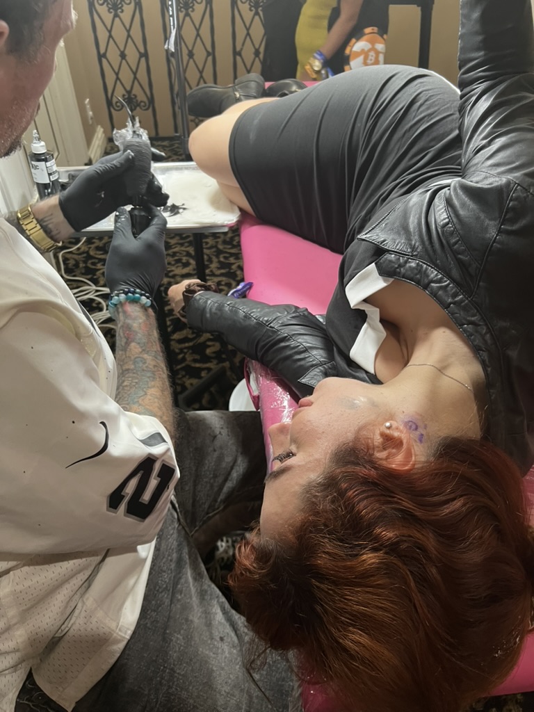 Joshua Cole tattoos neck on client lying on pink plastic-wrapped table — Joshua Cole offsite…, Work of Art Tattoo & Piercing, Las Vegas
