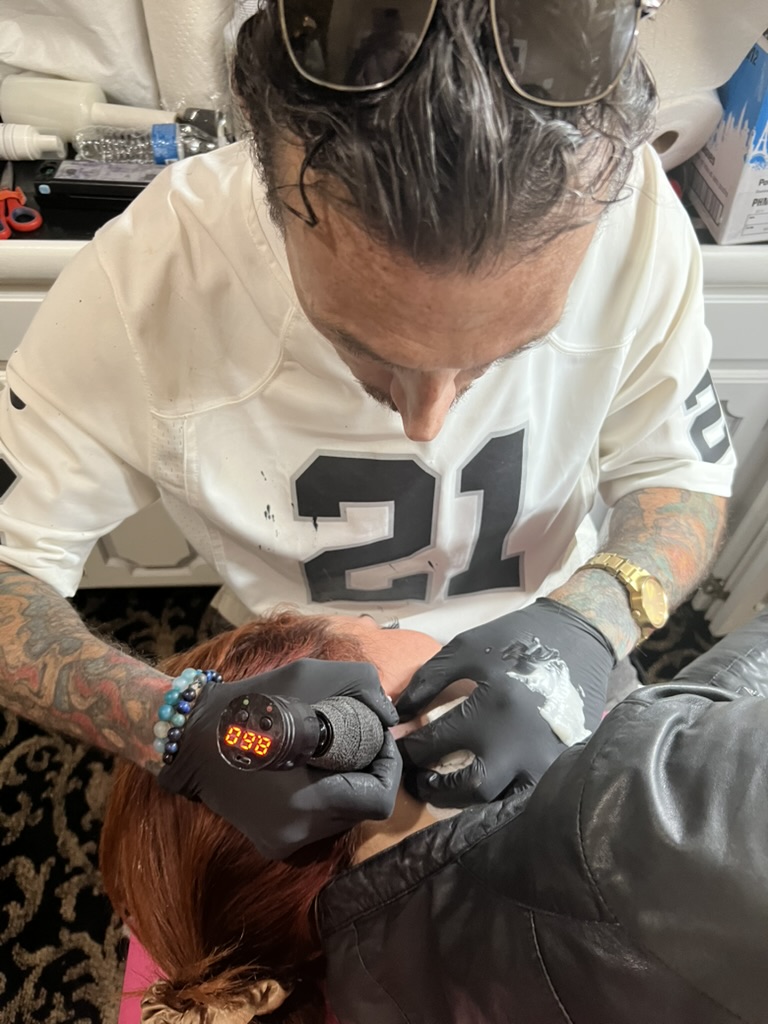 Overhead of Joshua Cole tattooing behind client's ear with rotary gun — Joshua Cole offsite…, Work of Art Tattoo & Piercing, Las Vegas