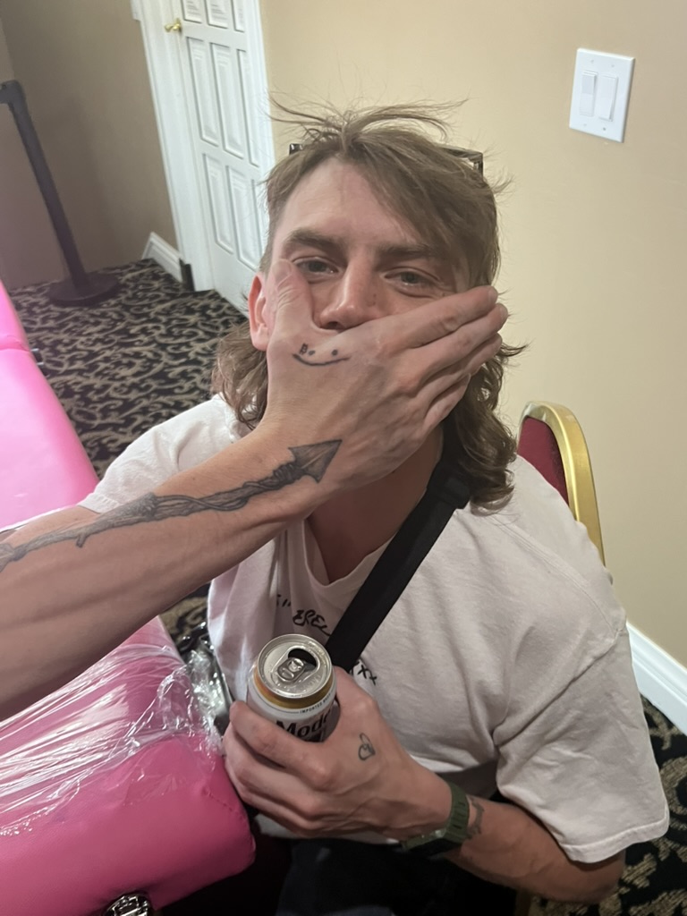 Smiley finger tattoo covers man's mouth; spear forearm and heart hand at offsite — Joshua Cole…, Work of Art Tattoo & Piercing, Las Vegas