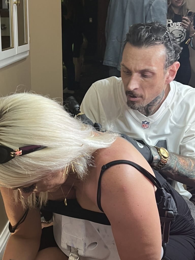 Joshua Cole tattoos upper back on blonde client leaning on portable chair at offsite — Joshua…, Work of Art Tattoo & Piercing, Las Vegas