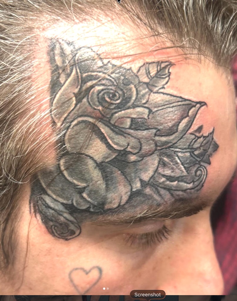 Soft-shaded black-grey rose tattoo on temple beside a small outline heart on cheek — Joshua…, Work of Art Tattoo & Piercing, Las Vegas