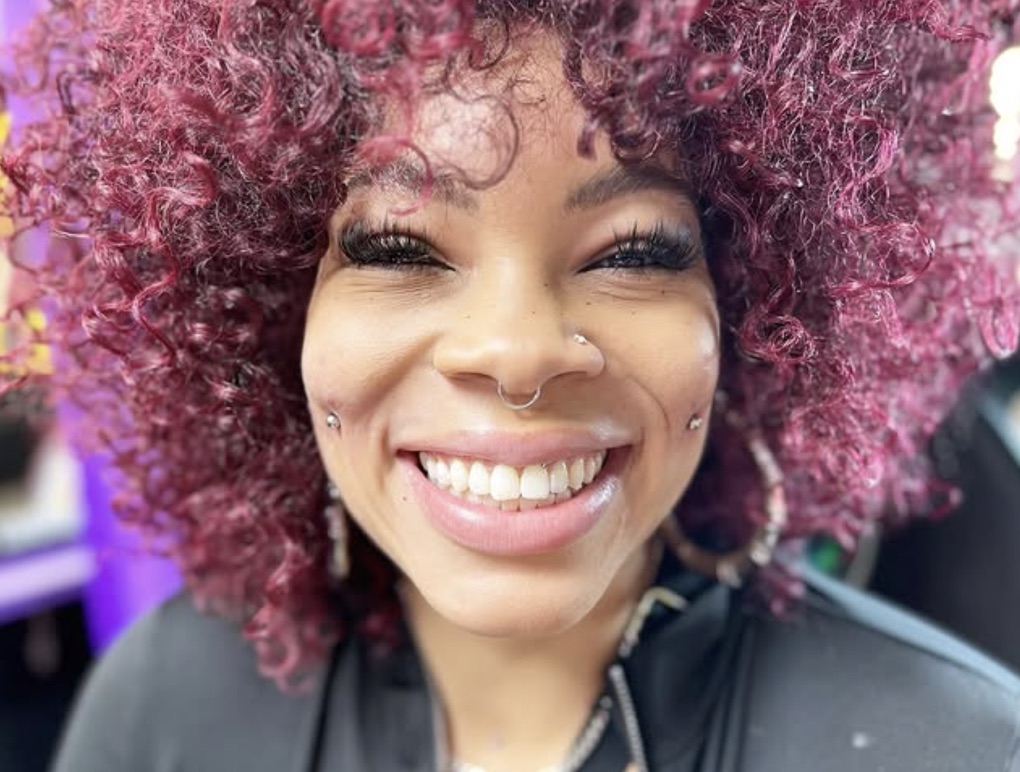 Smiling client with magenta curls, septum ring, nostril stud and cheek piercings — Joshua Cole…, Work of Art Tattoo & Piercing, Las Vegas