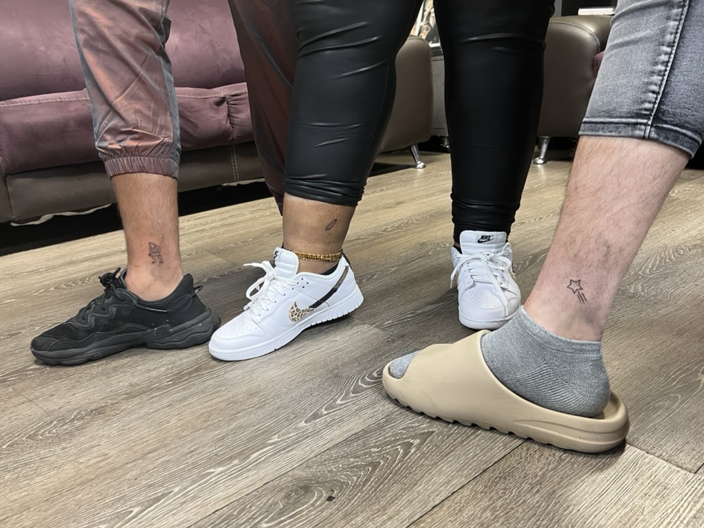 Three clients display fine-line ankle tattoos of a figure, pin, and star. — Joshua Cole, Work of…, Work of Art Tattoo & Piercing, Las Vegas