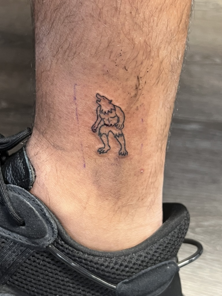 Fine-line howling werewolf outline tattooed above the ankle on lower leg. — Joshua Cole, Work of…, Work of Art Tattoo & Piercing, Las Vegas