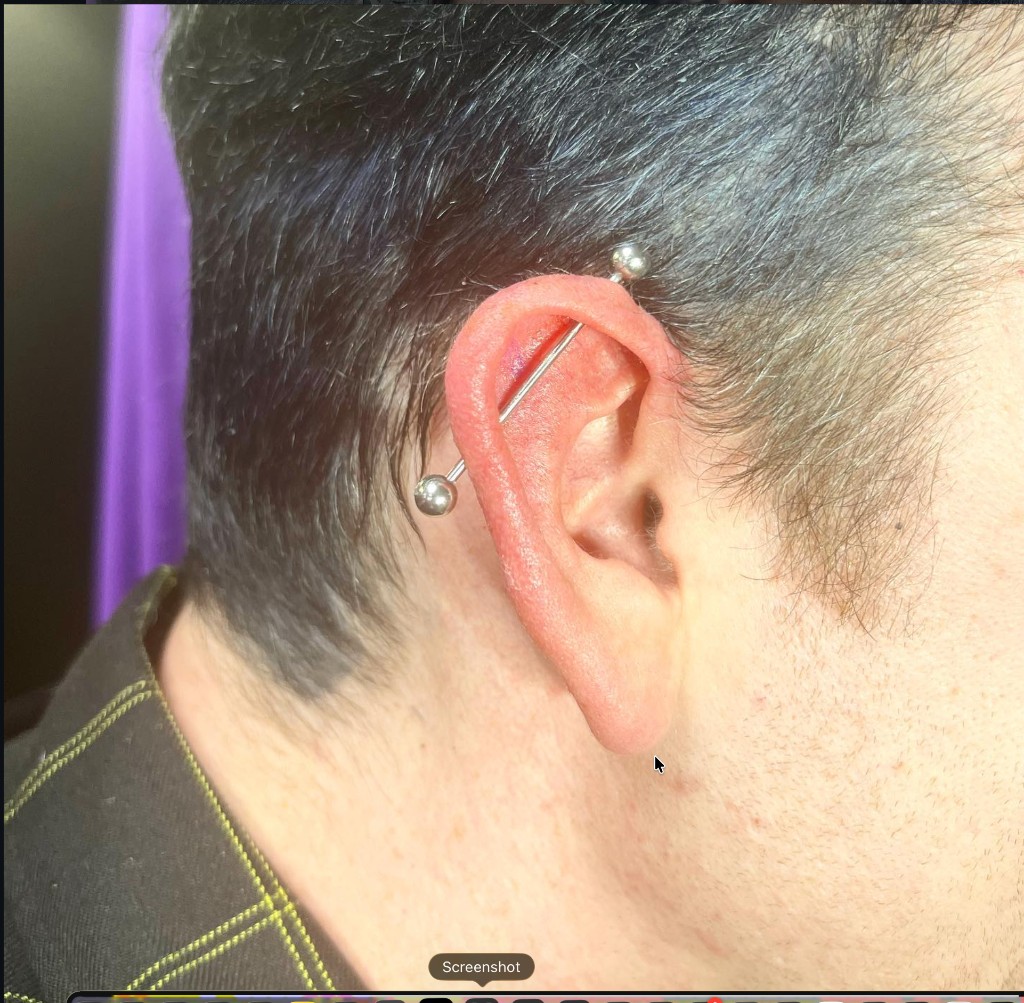 Silver industrial barbell through upper helix cartilage on short-haired client ear — Joshua…, Work of Art Tattoo & Piercing, Las Vegas