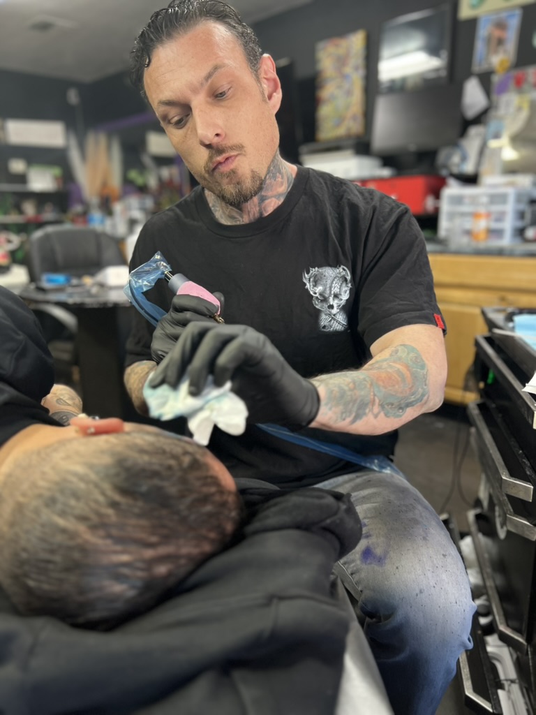 Joshua Cole carefully tattooing a client's temple during a head tattoo session. — Joshua Cole…, Work of Art Tattoo & Piercing, Las Vegas