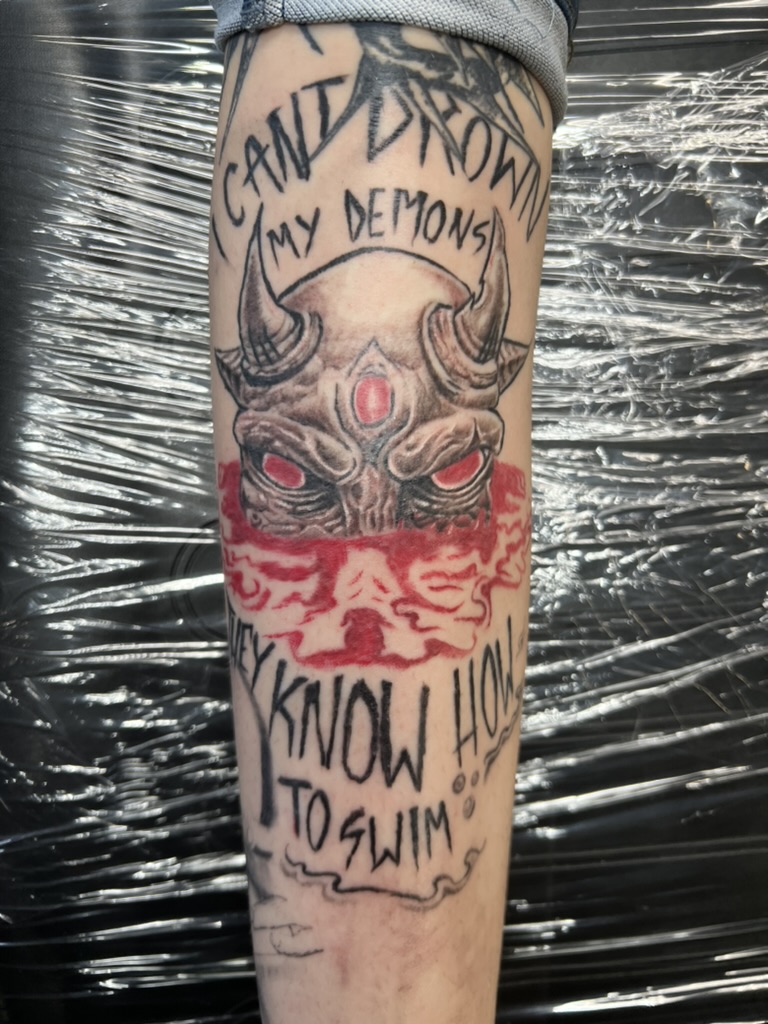 Illustrative three-eyed demon with lyric text — black, grey, and red by Joshua Cole, Work of Art…, Work of Art Tattoo & Piercing, Las Vegas